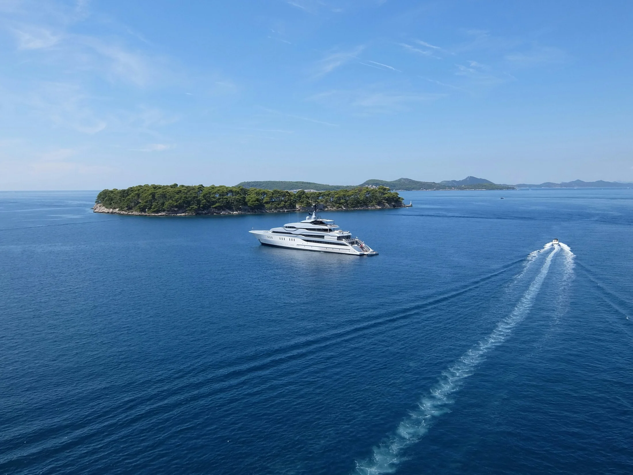 Superyachts on calm Mediterranean water, with islands on the horizon