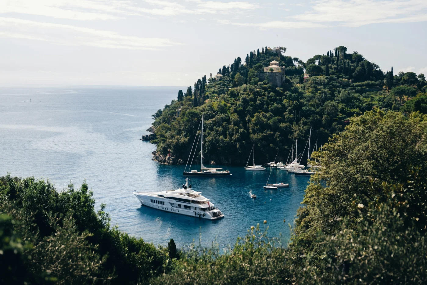 A sheltered bay and a yacht at rest beneath a wooded Mediterranean headland